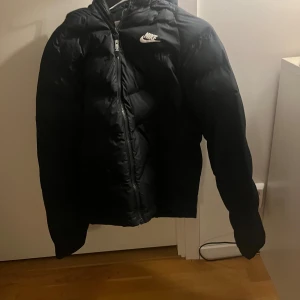 Svart pufferjacka från Nike - Säljer en svart pufferjacka från Nike. Jackan är i storlek 164 men passar från 158-172 kanske. Perfekt nu inför vinter. Denna jacka är i bra skick och har inga hål eller liknande. Skriv om ni är intresserade, priset är inte hugget i sten