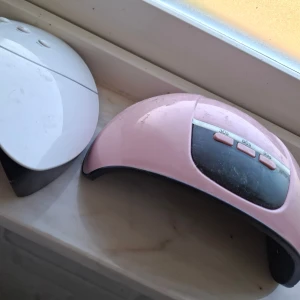 UV LED Nagellampa (2-pack) - Två UV LED-nagellampor för gelnaglar, en vit och en rosa. Båda har timerfunktioner (30/60/99/90/120 sekunder). Synligt ytslitage och damm, men knappar och funktioner ser intakta ut. Perfekt för hemmabruk eller salong.
