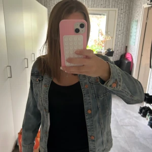 Ljusblå jeansjacka med knappar - Säljer en klassisk ljusblå jeansjacka med snygga sömmar och kopparfärgade knappar framtill. Jackan har två bröstfickor med lock och långa ärmar. 