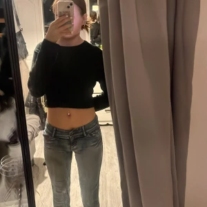 Blå jeans med mycket  detaljer - Säljer ett par blå jeans med coola detaljer på bakfickorna och ett inbyggt bälte bak.Jeansen har låg midja och utsvängda ben, med slitningar och tvättad look som ger en avslappnad vibe. Perfekt för dig som gillar streetstyle och vill sticka ut lite extra.