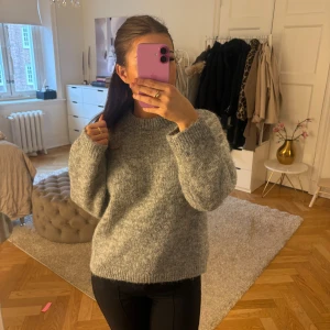 Grå stickad tröja från Gina Tricot - Mysig grå stickad tröja från Gina Tricot med rund halsringning. Tröjan har en lite loose fit och är perfekt för kyliga dagar. Den har ribbade muddar vid ärmslut och nederkant.