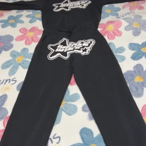 Svarta mjukisbyxor med tryck - Svarta mjukisbyxor med stort vitt och svart stjärntryck framtill. Byxorna har dragsko i midjan och är raka i modellen. Perfekta för chill eller träning, tillverkade i mjukt bomullsmaterial.