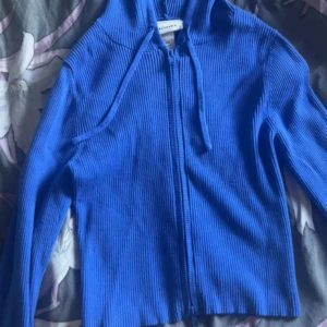 Blå ribbad hoodie från Monki - Säljer en blå ribbad hoodie från Monki i storlek XXS. Tröjan har dragkedja framtill, huva med snörning och är långärmad. Perfekt för dig som gillar en enkel men snygg look. Materialet är mjukt och stretchigt.