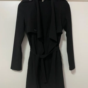 Svart trenchcoat med bälte från nelly - Svart tunn kofta från nelly, knappt använd, däremot finns en deffekt vid puffarna på axlarna men ingenting som syns! Nypris 399kr, pris går att diskuteras🤗 är i storlek xs/s!!
