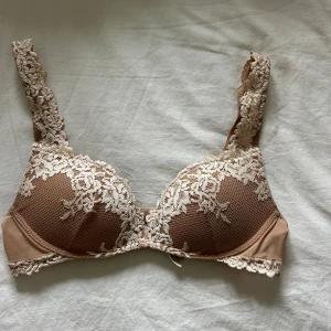 Beige spets-bh från Intimissimi 75C - Säljer en snygg beige bh från Intimissimi i storlek 75C. Bh:n har vackra spetsdetaljer i ljusbeige med blommönster över kuporna och axelbanden. Kuporna är vadderade och ger bra stöd. Perfekt för dig som gillar en feminin och elegant look.