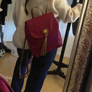 Vinröd ryggsäck från Tommy Hilfiger - Maroon/burgundy färgad Thommy Hilfiger ryggsäck. Perfekt för bland annat back to school! Super sött alternativ om man inte vill ha en ”sportig” ryggsäck. Köpt för flera år sedan men väldigt sparsamt använd! Skriv ett meddelande för fler interna bilder i väskan, mått eller vilka fack som finns.