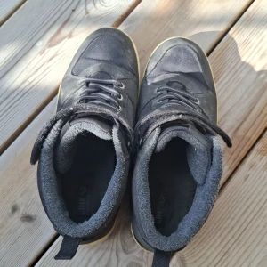 Svarta höga sneakers i storlek 38 - Svarta höga sneakers från Linear med snörning och kardborreband upptill. Ovandel i textil och syntet, insida fodrad för extra komfort. Sula i beige gummi med grovt mönster för bra grepp. Perfekta för dig som gillar streetstyle.