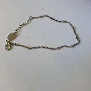 Tunt guldarmband med små detaljer - Snyggt och minimalistiskt armband i guldtonad metall med små diskreta kuldetaljer längs kedjan. Justerbar längd med karbinlås och rund bricka vid låset. Perfekt för dig som gillar stilrena smycken.