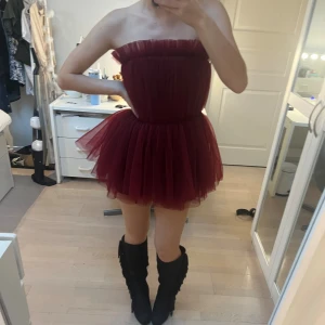 klänning - Supersöt vinröd kortklänning från H&M Edition i tyll med voluminös kjol och axelbandslös design. Perfekt för dig som vill sticka ut med en fluffig och trendig look. Klänningen har en markerad midja och romantiska volanger upptill.