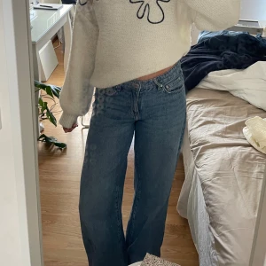 Blåa wide jeans med låg midja - Säljer ett par blåa jeans med låg midja och breda ben. Jeansen har klassisk femficksdesign, dragkedja och knapp framtill. Perfekta för dig som gillar en avslappnad och trendig look. Materialet är jeans i bomull. Använda sparsamt i ca 3 månader! Uppsydda men går att lägga ner igen!