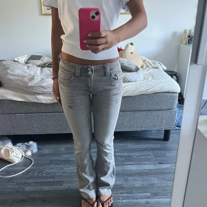 Grå bootcut jeans med hål - Snygga ljusgrå jeans med bootcut passform och slitna detaljer på benen. Byxorna har låg midja, klassiska fem fickor och coola bakfickor💕