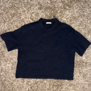 Mörkblå stickad tröja Gina Tricot XS - Mysig mörkblå stickad tröja från Gina Tricot i kortare modell med rund hals och korta ärmar. Tröjan är tillverkad i en mjuk blandning av akryl, polyester, ull, alpacka och elastan. Perfekt för lager-på-lager under kyliga dagar.