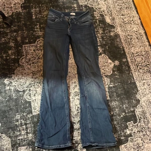 Blå bootcut jeans från Nelly - Snygga blå bootcut jeans från Nelly med låg midja och coola detaljer på bakfickorna. Jeansen har klassisk femficksdesign, markerade sömmar och är tillverkade i stretchigt denim för en bekväm passform. Perfekta för dig som gillar retrovibbar och vill sticka ut.