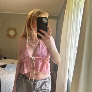 Rosa topp med knyt från SHEIN - Supersöt rosa linnetopp från SHEIN med crinklad struktur och volangkant. Toppen har smala knytband i offwhite, djup v-ringning och croppad passform. Perfekt för varma dagar och ger en chill vibe till din outfit.