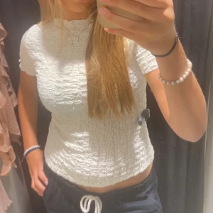 Vit smockad topp med kort ärm - Superfin vit topp med smockad struktur och korta ärmar. Hög halsringning och lätt croppad passform som sitter snyggt på kroppen. 