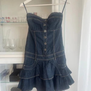 Jeansklänning med volanger från Fishbone - Supersöt axelbandslös jeansklänning från Fishbone, knappar framtill och volangkjol. Storlek S. prislapp kvar i nyskick