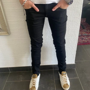 Tiger Of Sweden Jeans - Svarta slim fit jeans från Tiger of Sweden, tillverkade i Italien. Jeansen har klassisk femficksdesign, smal passform och stilren look. Perfekta för dig som gillar en tajt siluett och vill ha ett par svarta jeans som funkar till allt.