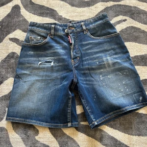 Blå jeansshorts från Dsquared2 - Snygga blå jeansshorts från Dsquared2 med slitna detaljer och coola slitningar framtill och baktill. Klassisk femficksmodell med knappgylf och Dsquared2-logga på etiketten. Shortsen är tillverkade i bomull med lite stretch för skön passform.