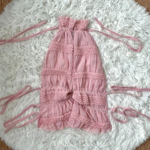 Söt rosa topp från SHEIN - Supersöt rosa korsett-topp från SHEIN med volangdetaljer och smockade partier. Sista bilden visa hur den ser ut på dig med slit i mitten. Passar storlek XS-S (32-36) och du kan justera hur ”tight” den ska vara vid midjan respektive byst.