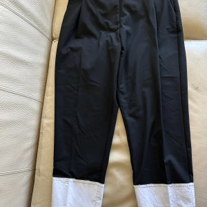 Svarta byxor med vit kant från Zara - Stilrena svarta byxor från Zara i storlek M med snygg vit kant längst ner på benen. Byxorna har en rak passform och är perfekta för dig som gillar en clean och modern look. Materialet känns mjukt och bekvämt mot huden.