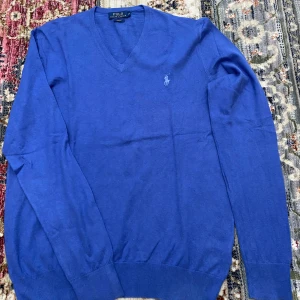 Tröja Polo Ralph Lauren - Slim fit blå v-ringad tröja från Polo Ralph Lauren med broderad logga på bröstet. Tröjan är långärmad och tillverkad i mjuk ull.