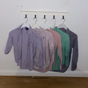Ralph Laurent skjortor bulk x5  - Flera skjortor från Ralph Lauren i olika färger och mönster. Två randiga skjortor i lila och rosa toner samt två rutiga skjortor i grönt och marinblått. Alla har klassisk krage, knappar framtill och lång ärm. Perfekt för dig som gillar preppy och färg.