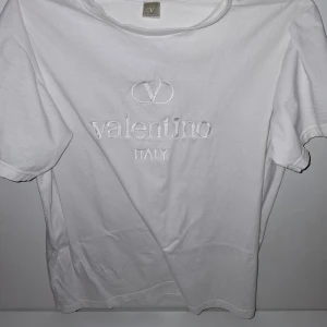 Vit t-shirt från Valentino - Vit t-shirt från Valentino med broderad logga och texten 'Italy' på bröstet. Klassisk rund hals och korta ärmar. Mjuk och skön bomull som passar perfekt till jeans eller shorts. Snygg och stilren design med exklusiv känsla.