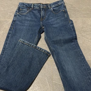 Mörkblå jeans Mira W25 L30 - Snygga mörkblå jeans från Mira med klassisk femficksdesign och raka ben. Jeansen har kontrastsömmar och är låg midjade, perfekta till vardagslooken. Materialet är slitstarkt denim i bomull för en tidlös stil.