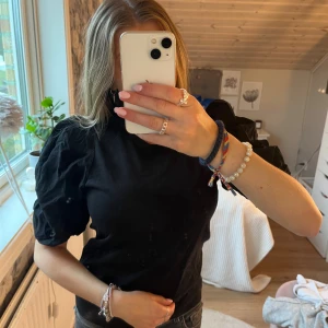 Svart topp med puffärm från Kappahl - Svart topp från Kappahl med trendiga puffärmar och rund halsringning. Modellen är enkel men har coola voluminösa ärmar som ger en snygg siluett. Perfekt att styla med jeans eller kjol för en uppdaterad look. Aldrig använd 