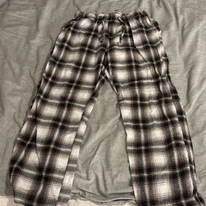 Rutiga mjukisbyxor med snörning - Säljer ett par rutiga mjukisbyxor i brunt, svart och vitt. Byxorna har resår och snörning i midjan för skön passform. Perfekta för chill dagar hemma eller när du vill vara extra bekväm. Tillverkade i mjukt bomullstyg.