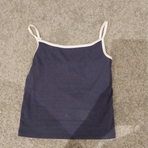 Mörkblå linnetopp med vita kanter - Supersöt mörkblå linnetopp från Sister med tunna, justerbara axelband och vita kontrastkanter. Enkel och stilren design som passar perfekt till jeans eller kjol. Mjuk och skön bomullskänsla, perfekt för varma dagar.