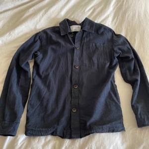 Mörkblå overshirt från Selected Homme - Stilren mörkblå overshirt från Selected Homme med klassisk krage, bröstficka och knäppning framtill. Skjortan är tillverkad i mjuk bomull och har långa ärmar med knapp vid ärmslut. Perfekt att bära öppen eller stängd för en avslappnad look.