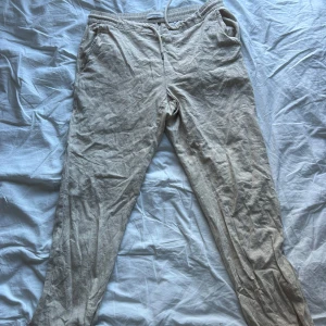 Beiga linnebyxor från Dressmann L - Snygga beiga linnebyxor från Dressmann i storlek L. Byxorna har elastisk midja med snörning, sidfickor och bakfickor. Perfekta för en chill och avslappnad stil under varmare dagar. Materialet är en linneblandning som ger en luftig känsla.