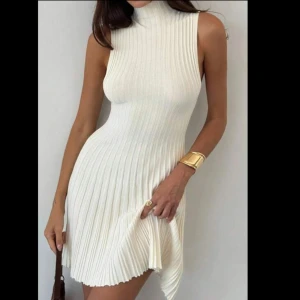 Vit ribbad kortklänning med hög krage - Supersnygg vit kortklänning med ribbad struktur och plisserad kjol. Klänningen är ärmlös och har en hög krage som ger en clean och modern vibe. Materialet är stickat och stretchigt, vilket gör att den sitter riktigt bra.💕