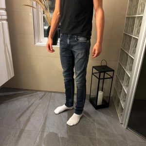Replay Anbass  - Snygga Replay Anbass jeans i 29/32 mörkblå tvätt med slitningar och klassisk femficksdesign. Modellen är slim fit med smal passform och raka ben. Jeansen har låg midja och är tillverkade i stretchig bomullsdenim för extra komfort.