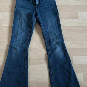 Blå bootcut jeans från Lindex - Snygga blå jeans från Lindex i klassisk bootcut-modell. Jeansen har normal passform, resår i midjan baktill och femficksdesign. Tillverkade i mjukt denimtyg med lätt slitning för en cool look.