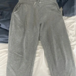 Grå mjukisbyxor från GANT, strl S - Grå mjukisbyxor från GANT med dragsko i midjan och ribbade muddar. Byxorna har fickor fram och en bakficka, samt GANT-logga broderad vid ena fickan. Perfekta för chill dagar och riktigt sköna tack vare mjukt bomullsmaterial.