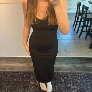 Svart långklänning med slits från Bershka  - Säljer en svart långklänning med smala axelband och liten slits baktill. Klänningen har en figurnära passform och är tillverkad i ett mjukt, stretchigt material. Snygg v-ringning och diskreta rosetter vid axelbanden ger en extra touch. Storlek S, men passar mig som är M. Nästan lite satinliknande material så den ser väldigt elegant ut. 🌸