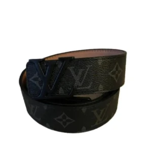  Louis Vuitton bälte  - Snyggt svart bälte från Louis Vuitton med klassiskt monogrammönster och stor LV-logga i metall som spänne. Bältet har en lyxig känsla och är tillverkat i skinn med mörka detaljer. Perfekt accessoar för att lyfta din outfit.