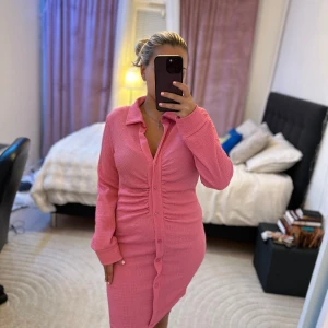 Rosa ribbad skjortklänning med knappar - Säljer en rosa skjortklänning med lång ärm och knappar hela vägen framtill. Klänningen har en krage, ribbad struktur och figurnära passform. Perfekt för dig som gillar en stilren men ändå trendig look.