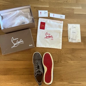 Christian Louboutin grå mockasneakers - Snygga grå sneakers från Christian Louboutin i mocka med klassisk röd sula och vita kanter. Skorna har rund tå, snörning och diskreta metalldetaljer på sidan. Kommer med originalkartong, dustbag och äkthetsbevis. Perfekt för dig som gillar exklusiva och stilrena sneakers. Storlek 45 men passar även 44. Pris kan diskuteras. 