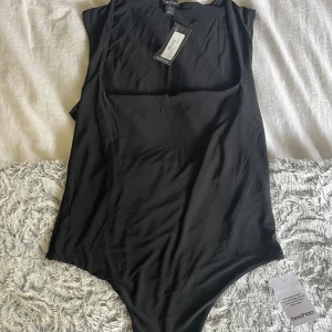 Svart body  från Boohoo - Enkel och stilren svart body från Boohoo i klassisk modell. Tillverkad i ett mjukt och stretchigt syntetmaterial som sitter skönt på kroppen. Aldrig använd 