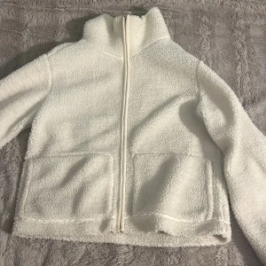 Vit teddyjacka från 157, storlek M - PRIS KAN DISKUTERAS!                                     Mysig vit teddyjacka från 157 i storlek M. Jackan har hög krage, två stora fickor framtill och hel dragkedja. Perfekt för kalla dagar när du vill ha en chill och fluffig look. Materialet är mjuk fleece som känns skönt mot huden.