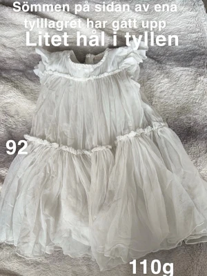 Vit tyllklänning med volanger - Supersöt vit klänning i tyll med flera lager och volangdetaljer. Klänningen har korta ärmar och rund halsringning, perfekt för speciella tillfällen. Lätt och fluffig känsla som ger en drömmig look.🌸 Litet hål i tyllen. Sömmen på ena lagret till har gått upp. Storlek 92