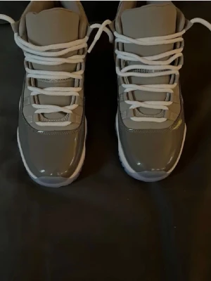 Nike Air Jordan 11 Cool Grey sneakers - Säljer ett par Nike Air Jordan 11 Cool Grey sneakers med högt skaft. Skorna har en snygg grå färg med vita detaljer och snörning. Ovandelen är i en mix av blankt och matt material, och sulan är vit med isblå inslag. Perfekta för dig som gillar klassiska och stilrena sneakers. Helt nya och aldrig änvänt dom 