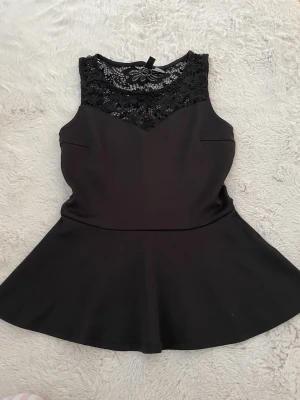 Svart kort klänning med spetsdetaljer - Supersnygg svart klänning med utställd kjol och ärmlös design. Överdelen har vackra spetsdetaljer både fram och bak som ger en elegant touch. Perfekt för dig som vill ha något stilrent men ändå med det lilla extra.