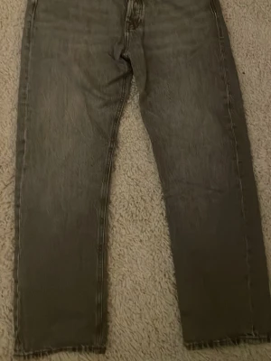 Grå jeans från Jack & Jones - Säljer ett par grå jeans från Jack & Jones med klassisk femficksdesign och raka ben. Jeansen har en snygg tvättad look och metallknapp i midjan. Perfekta för dig som gillar en enkel och stilren stil. Storlek 30:30