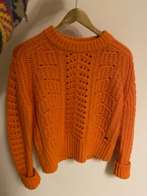 Orange stickad tröja från edc - Säljer en orange stickad tröja från edc i storlek M. Tröjan har ett grovt, öppet stickat mönster framtill och på ärmarna, samt ribbade muddar vid hals, ärmslut och nederkant. Perfekt för dig som gillar färgstarka och mysiga plagg.