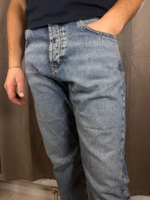 Levi's 501 ljusblå raka jeans - Klassiska Levi's 501 jeans i ljusblå tvätt med raka ben och knappgylf. Jeansen har fem fickor, orange sömmar och den ikoniska röda Levi's-lappen vid bakfickan. Tillverkade i slitstarkt bomullsdenim för en tidlös look.