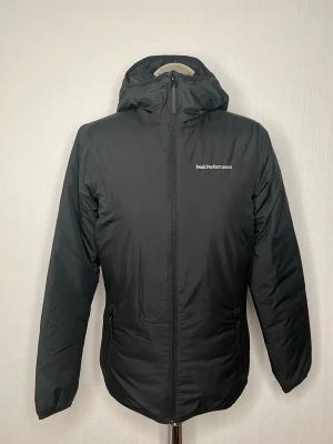 Svart pufferjacka Peak Performance S - Säljer en svart pufferjacka från Peak Performance i storlek S. Jackan har huva, hel dragkedja framtill och två sidofickor med dragkedja. Diskret logga på bröstet och innerficka med dragkedja. Perfekt för kyliga dagar och enkel att matcha. Enbart använd en gång. 